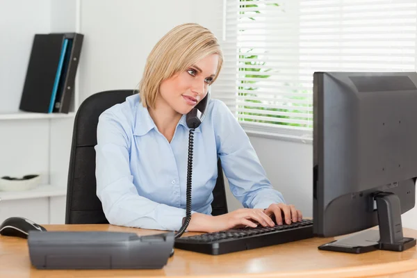 Mulher de negócios trabalhando no telefone enquanto digita — Fotografia de Stock