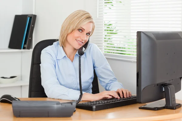 Working businesswoman on the phone while typing looks into camer — Stock Photo, Image
