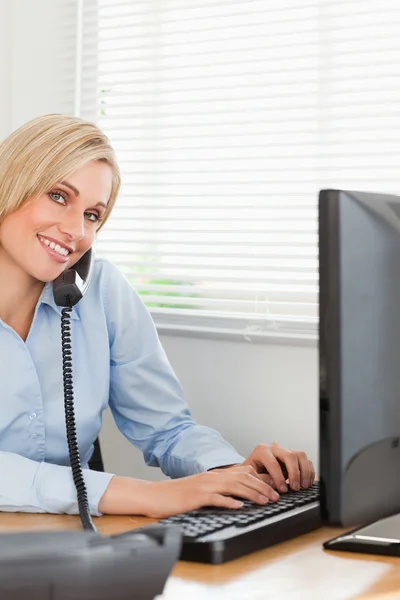 Charming blonde businesswoman on the phone while typing looks in — Stock Photo, Image