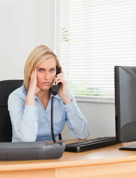 Rubia mujer de negocios en el teléfono mientras tiene dolor de cabeza mira en c —  Fotos de Stock