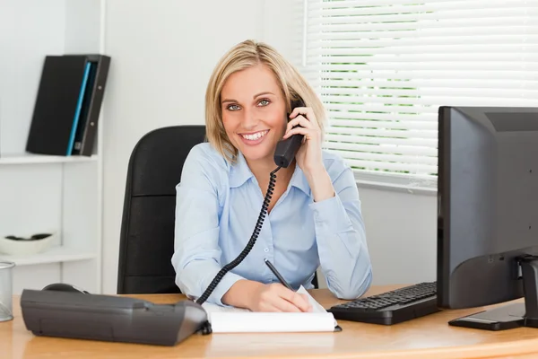 stock image Cute businesswoman on phone writing something down looks into ca