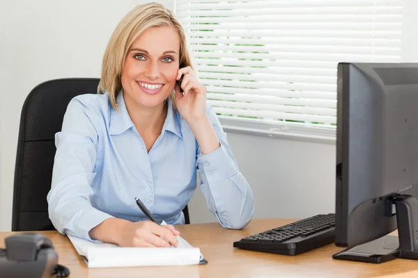 Cute blonde businesswoman on mobile writing something down looks — Stock Photo, Image