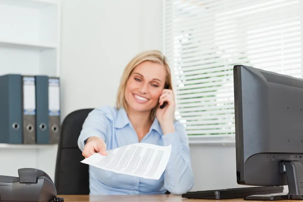 Smiling businesswoman phoning and passing a paper looks into cam — Stock Photo, Image