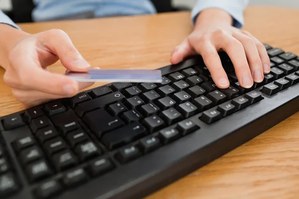 Mujer escribiendo en el teclado sosteniendo una tarjeta de crédito — Foto de Stock