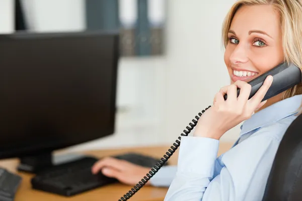 Junge blonde Geschäftsfrau lächelt in die Kamera, während sie am Telefon ist — Stockfoto