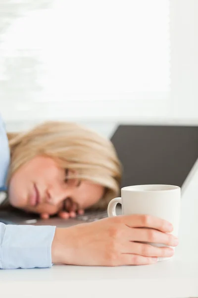 Prachtige blonde vrouw slapen op haar laptop houden kopje coff — Stockfoto