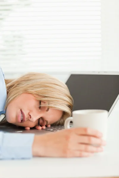 Preciosa mujer rubia durmiendo en su cuaderno sosteniendo taza de co —  Fotos de Stock