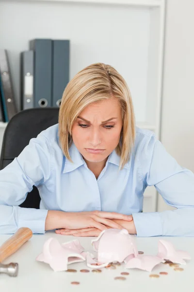 Sulking woman sitting in front of an shattered piggy bank — Stock Photo, Image