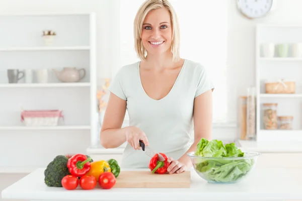 Ung kvinna skära grönsaker ler in i kameran — Stockfoto