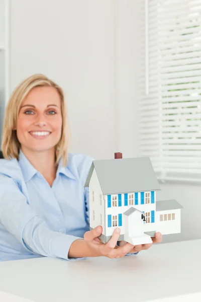 Leende affärskvinna visar modell hus ser in i kameran — Stockfoto