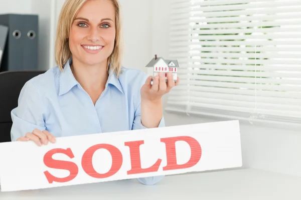 Блондинка-бизнесвумен, показывающая миниатюрный дом и знак "Продано" — стоковое фото