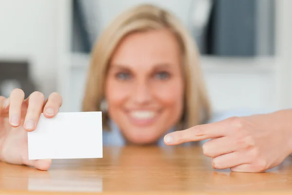 Empresária apontando para um cartão agachado atrás de sua mesa olha — Fotografia de Stock