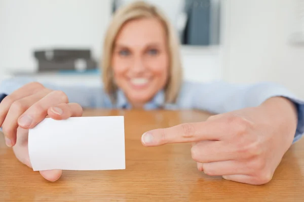 Blonde businesswoman pointing at a card crouching behind her des — Stock Photo, Image