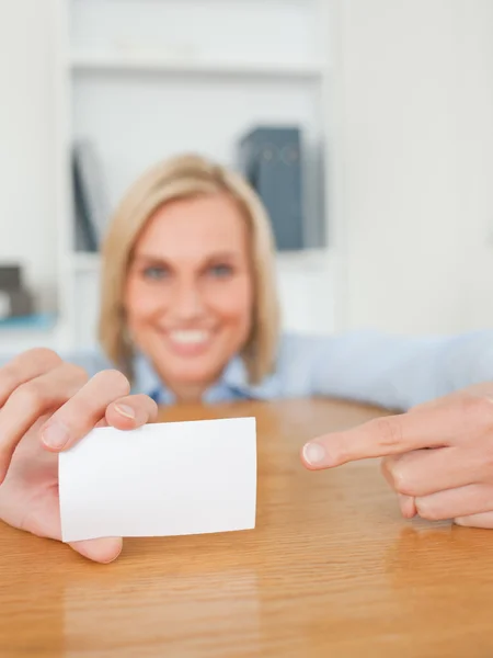 Blonde smiling businesswoman pointing at a card crouching behind — Stock Photo, Image