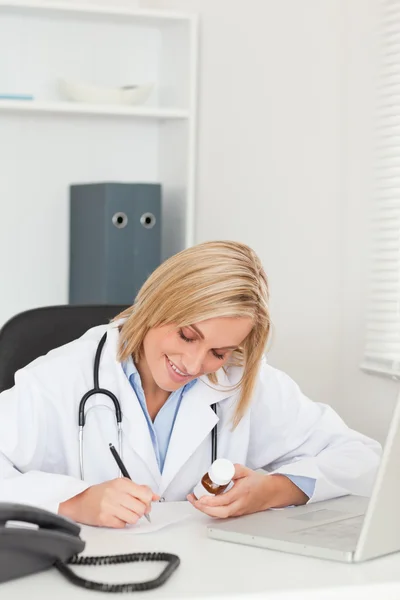 Médico escrevendo algo enquanto segurava a medicina — Fotografia de Stock