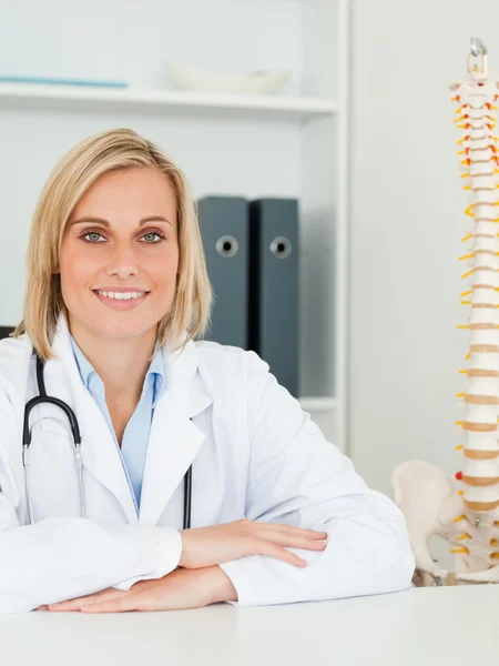 Médico sonriente con la columna vertebral modelo al lado de su mira a la cámara —  Fotos de Stock