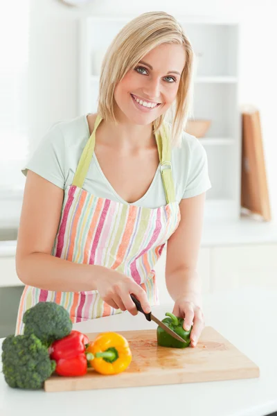 Gorgeous woman cutting green pepper looks into camera — Stock Photo, Image