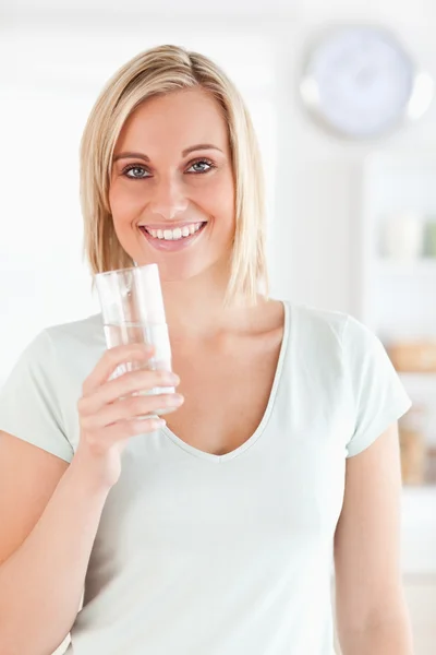 Lachende vrouw met glas water ziet er in camera — Stockfoto