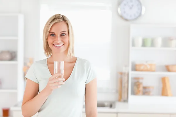 Encantadora mujer sosteniendo vidrio lleno de agua mientras está de pie lo — Foto de Stock