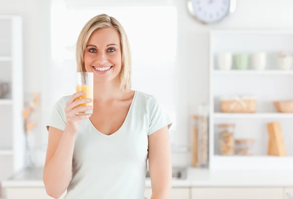 Affascinante donna in possesso di vetro pieno di succo d'arancia mentre stan — Foto Stock