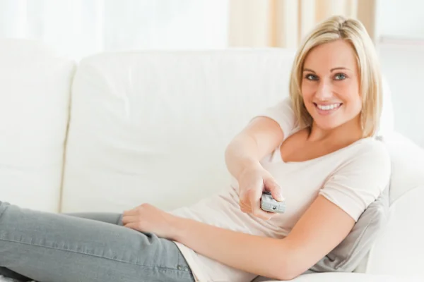 Woman wijzend een afstandsbediening op de camera met een weten glimlach — Stockfoto