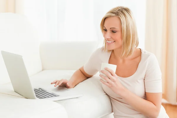 Bir dizüstü bilgisayar kullanırken bir kupa tutan kadın — Stok fotoğraf