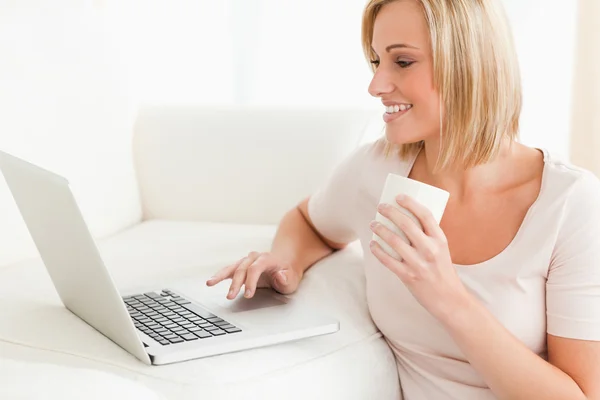 Bir dizüstü bilgisayar kullanırken bir kupa tutan bir kadın, yakın çekim — Stok fotoğraf