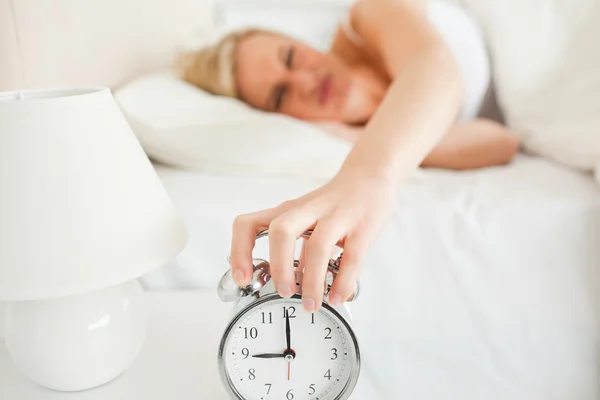 Upset woman switching off her alarm clock — Stock Photo, Image