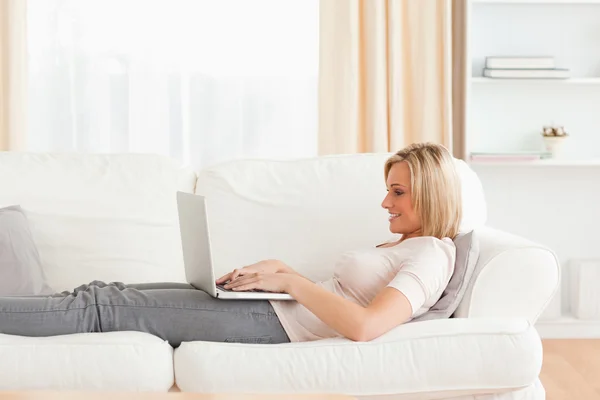 Mulher usando um laptop enquanto deitado em um sofá — Fotografia de Stock