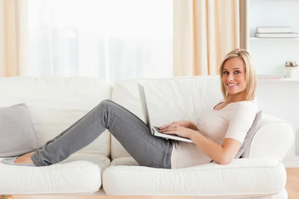 Sevimli kadın kanepede yatarken bir dizüstü bilgisayar ile — Stok fotoğraf