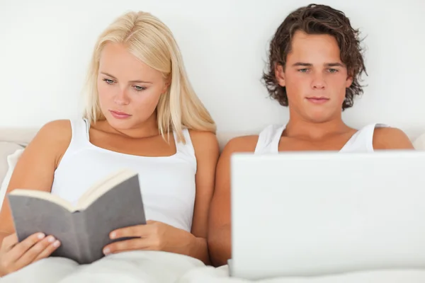 Женщина читает книгу, пока ее парень пользуется ноутбуком — стоковое фото
