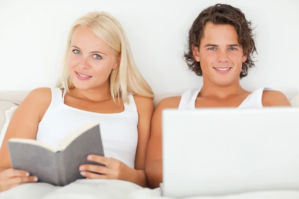 用一台笔记本电脑，虽然他的女朋友读一本书的人 — 图库照片