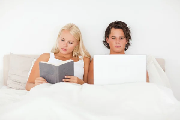 使用一台笔记本电脑，虽然他的女朋友读一本书的人 — 图库照片