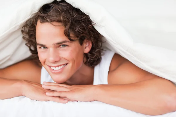 Человек под одеялом с знающей улыбкой — стоковое фото