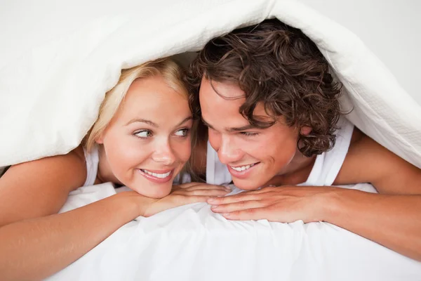 Paar unter einer Bettdecke mit einem wissenden Lächeln — Stockfoto
