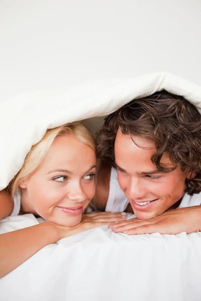 Retrato de una pareja bajo un edredón con una sonrisa sabia —  Fotos de Stock
