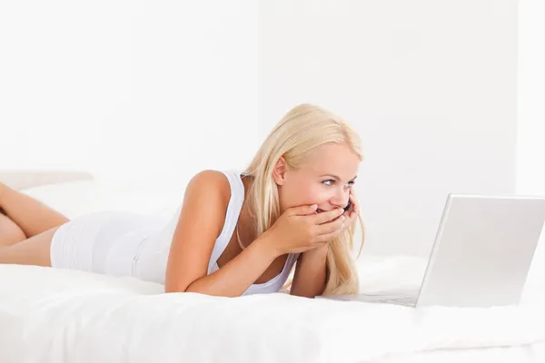 Kadın telefonda bir dizüstü bilgisayar kullanırken gülüyor — Stok fotoğraf
