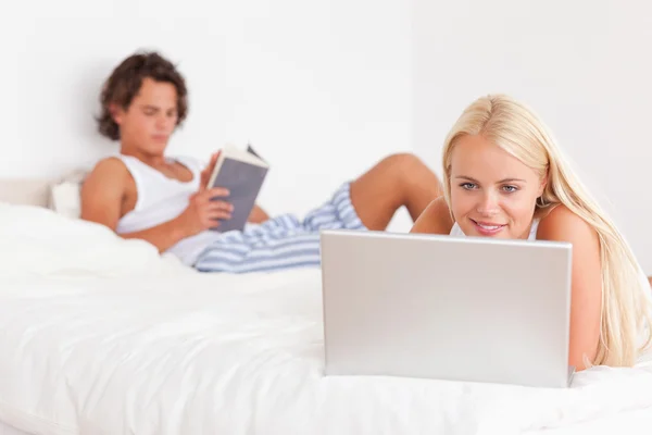 使用一台笔记本电脑，而她的未婚夫正在读取的女人 — 图库照片