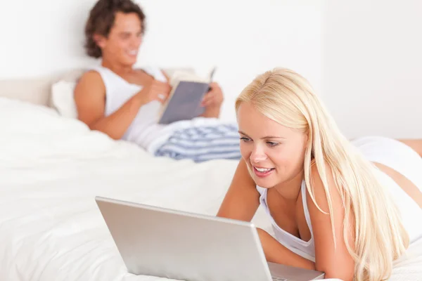 Kvinna med en bärbar dator medan hennes fästman läser — Stockfoto