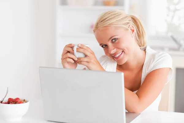 Mulher tomando uma xícara de café enquanto usa seu laptop — Fotografia de Stock