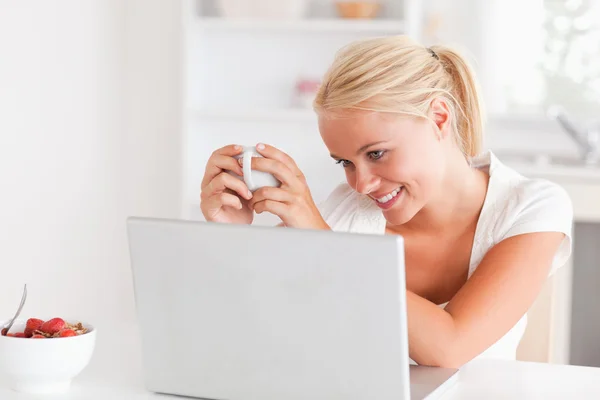 Mulher tomando uma xícara de chá enquanto usa seu laptop — Fotografia de Stock