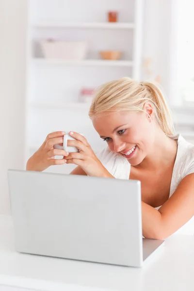 Retrato de una mujer tomando una taza de té mientras usa su computadora portátil —  Fotos de Stock
