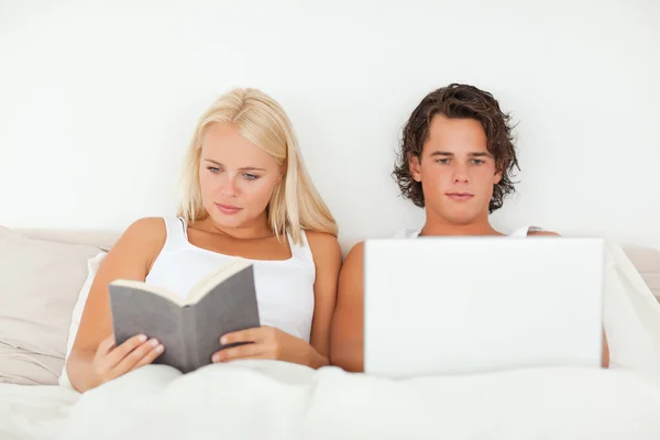 女性は彼女のボーイ フレンドは、ラップトップを使用している間本を読んで — ストック写真