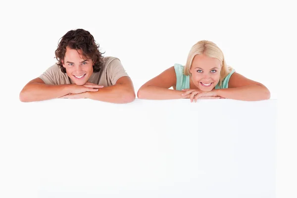 Smiling couple leaning on a whiteboard — Stock Photo, Image