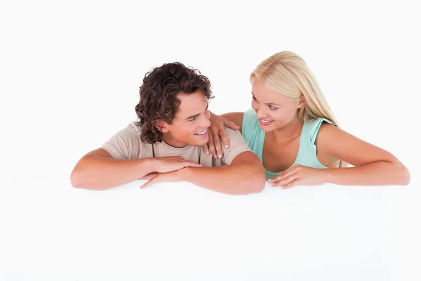 Bonito casal feliz inclinado em um quadro branco — Fotografia de Stock