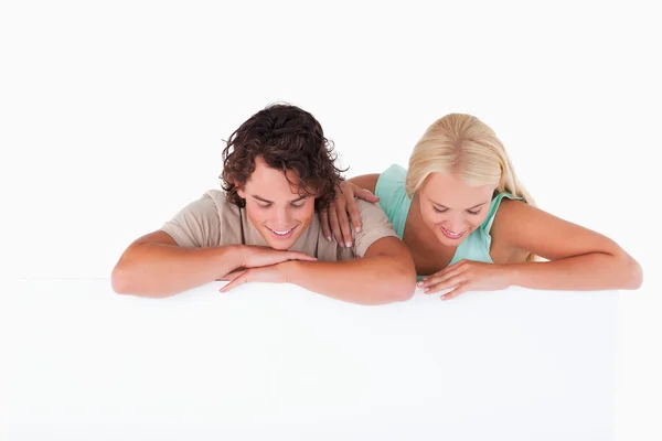 Bonito casal sorrindo encostado em um quadro branco — Fotografia de Stock