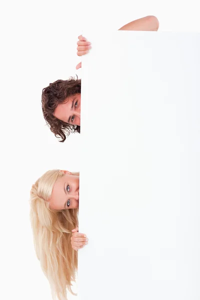 Söta par gömmer sig bakom en whiteboard — Stockfoto