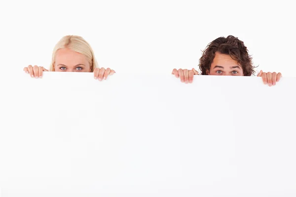 Happy Couple hiding behind a whiteboard — Stock Photo, Image