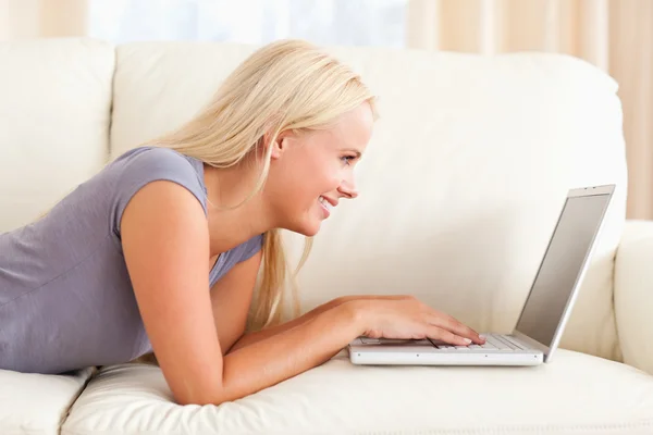 Kobieta, leżąc na kanapie przy przy pomocy pewien laptop — Zdjęcie stockowe