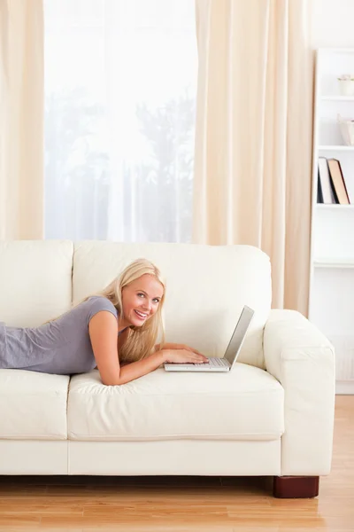 Porträtt av en kvinna liggande på en soffa med en bärbar dator — Stockfoto